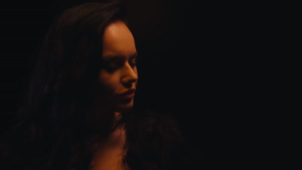 mujer sexy en abrigo de piel sintética ajustando el cabello aislado en negro - Imágenes, Vídeo