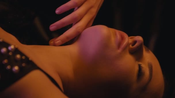 mujer joven en sujetador sexy tocando el cuello sobre fondo oscuro - Imágenes, Vídeo