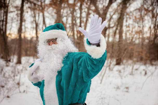 Walking through the winter forest, elf in green suit dress waves his hand carrying Christmas gift presents - Photo, Image