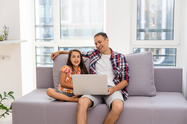自宅のソファに座っている間、技術を使用して子供と幸せな家族 - 写真・画像