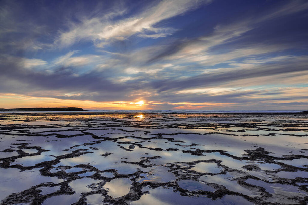 Прекрасний захід сонця над океаном з кам'янистим пляжем і припливними басейнами на передньому плані
 - Фото, зображення