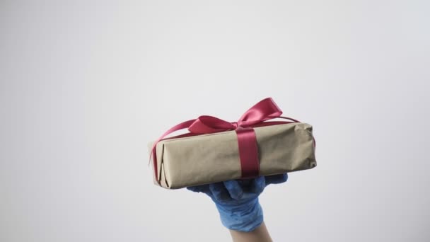 рука в синей защитной перчатке дает подарочную коробку с лентой. КОВИД-19 Рождество - Кадры, видео