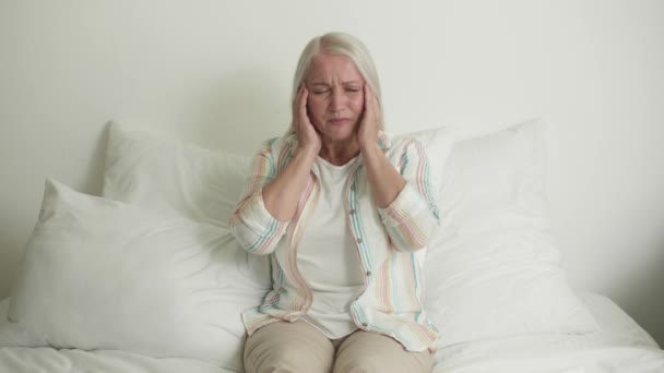 Mujer madura estresada que sufre de dolor de cabeza en el dormitorio - Metraje, vídeo