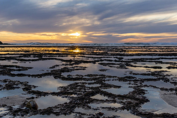 Прекрасний захід сонця над океаном з кам'янистим пляжем і припливними басейнами на передньому плані
 - Фото, зображення