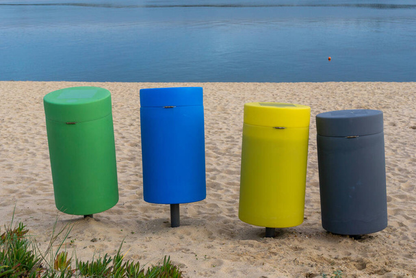 Τέσσερις πολύχρωμοι κάδοι ανακύκλωσης σε μια αμμώδη παραλία - Φωτογραφία, εικόνα
