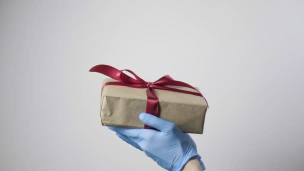 gros plan sur les mains dans des gants de protection bleus tenant boîte cadeau avec ruban rouge - Séquence, vidéo