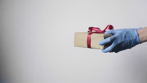 Nahaufnahme an den Händen in blauen Schutzhandschuhen mit Geschenkbox mit roter Schleife - Filmmaterial, Video