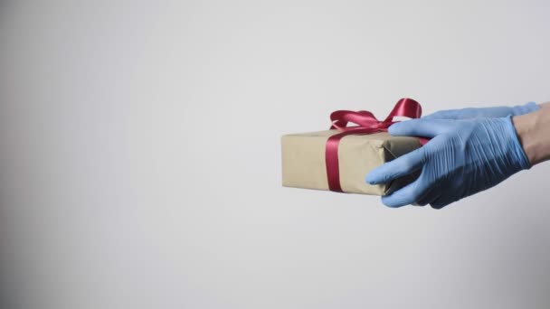 Hände in blauen Schutzhandschuhen überreichen dem Kind ein Weihnachtsgeschenk mit roter Schleife - Filmmaterial, Video