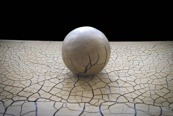alegorie: koule z hlíny je naše planeta umístěná na povrchu dobrého tvrdého povrchu s prasklinami, připomínajícími ekologickou katastrofu - Fotografie, Obrázek