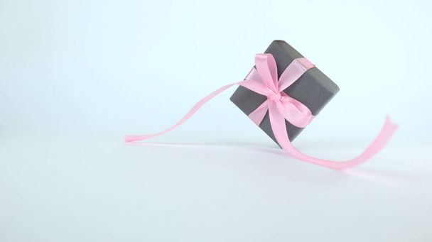 Une petite boîte grise avec un arc rose. Isolé sur fond blanc. Place pour ton texto. Espace de copie. - Photo, image