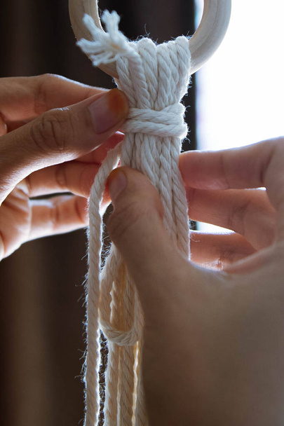 Nahaufnahme einer jungen Frau, die mit der Hand das Seil spannt, um Makrame zu machen - Foto, Bild