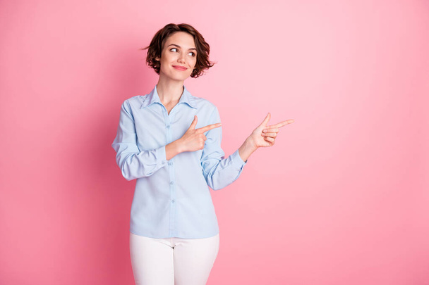 Photo of attractive charming lady direct fingers side empty space show discount banner interested shopper wear blue office shirt white pants isolated pink pastel color background - Photo, image