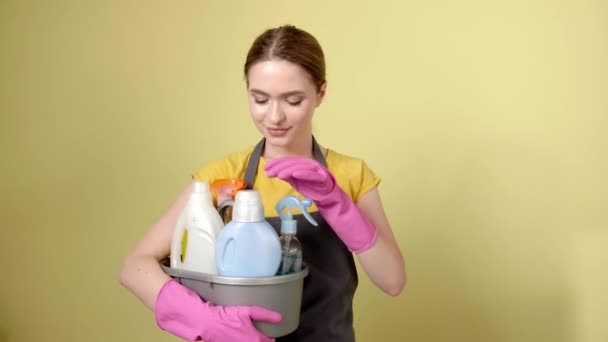 Jeune femme avec ensemble de fournitures de nettoyage sur fond de couleur - Séquence, vidéo