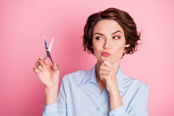 Closeup photo of attractive doubtful lady hold professional scissors look minded not sure about cut hair changing style contemplation wear blue shirt isolated pink pastel color background - Photo, Image