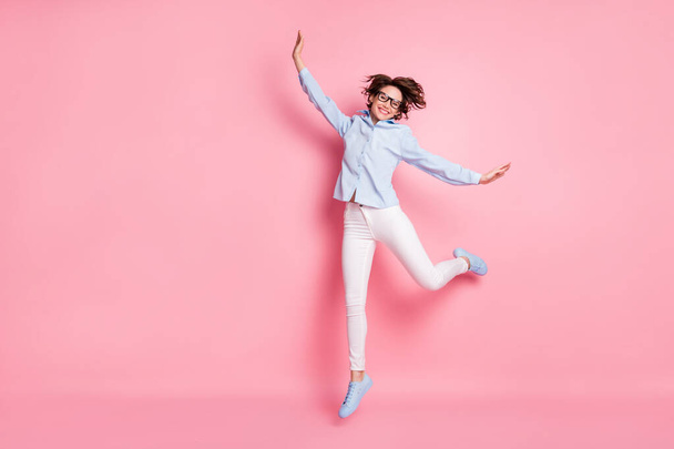 Full size photo of pretty lady toothy smiling good mood jump high up air flight carefree easy-going student person wear blue shirt white pants shoes isolated pink color background - Photo, image