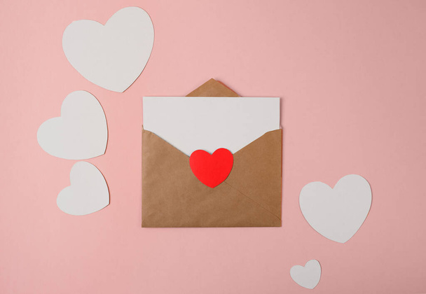 Craft envelope with blank white note mockup inside and Valentines hearts on pink background. Flat lay, top view. Romantic love letter for Valentine's day concept. - Foto, immagini