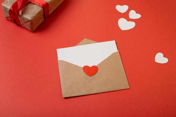 Craft envelope with blank white note mockup inside and Valentines hearts on red background. Flat lay, top view. Romantic love letter for Valentine's day concept. - Valokuva, kuva