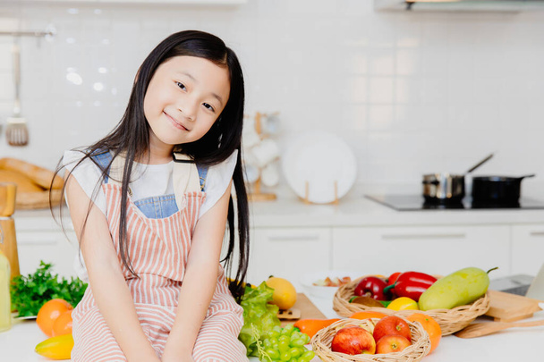 Portrét malá roztomilá dívka sedící na stole kuchyně na pozadí - Fotografie, Obrázek