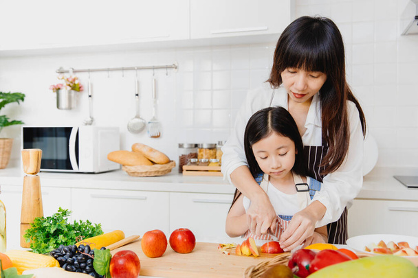 Mère asiatique enseignant son petit enfant à l'aide d'un couteau pour trancher la pomme pour cuisiner la nourriture dans la cuisine. - Photo, image