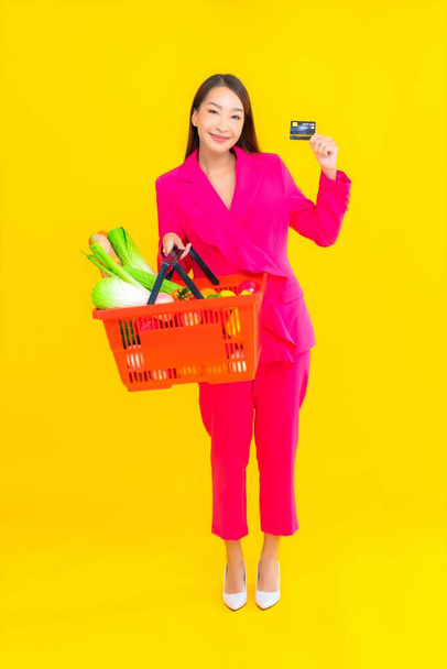色の背景にスーパーマーケットからバスケットやカートや食料品と肖像画の美しい若いアジアの女性 - 写真・画像