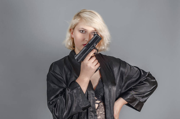 Chica rubia sosteniendo un arma en la mano cerca de su cara. Amenaza, crimen, protección. - Foto, Imagen