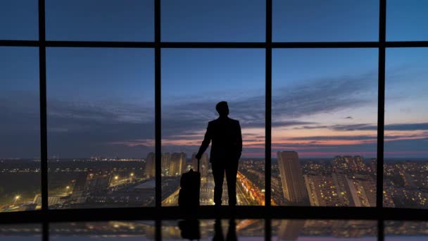 Ο άνθρωπος με τη βαλίτσα στέκεται κοντά στο παράθυρο στο φόντο της πόλης νύχτα. Λήξη χρόνου - Πλάνα, βίντεο