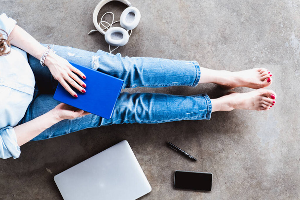Ragazza in jeans seduta sul pavimento a casa con notebook, laptop, telefono, penna e cuffie - Foto, immagini