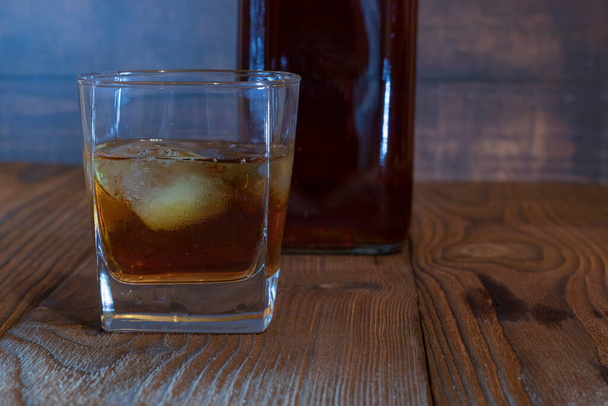Whisky s ledem ve sklenici na starém dřevěném pozadí. Whisky s ledem ve sklenici. Whisky nebo koňak. Selektivní zaměření. - Fotografie, Obrázek