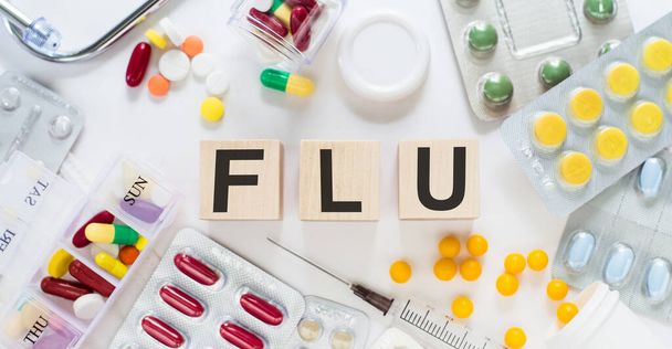 FLU. Word on wooden blocks on a desk. Medical concept with pills, vitamins, stethoscope and syringe on the background. - Foto, imagen