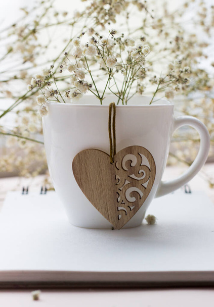 wooden heart and white porcelain Cup with a bouquet of small white flowers on a light background - Photo, Image