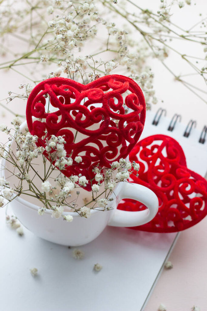 kırmızı kalp ve beyaz porselen kupa açık arkaplanda küçük beyaz çiçekler. - Fotoğraf, Görsel