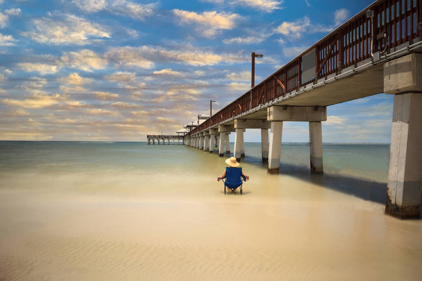 Sunset over Lone woman relaxing beside the Boardwalk of the Fort Myers Pier on Fort Myers Beach, Florida - Photo, Image