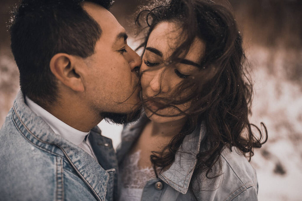 デニムジャケットのメキシコのヒスパニック系男性が特大と女性は巨大な笑いキスをしています。新郎新婦の結婚式は雪の中で冬のカップルを愛しています。おしゃれなパーティウェディングウェア2021 - 写真・画像
