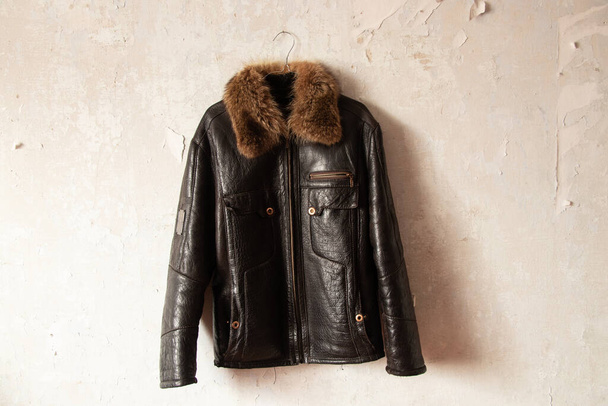 black leather winter men's jacket hanging on a hanger on the wall indoors - Photo, Image