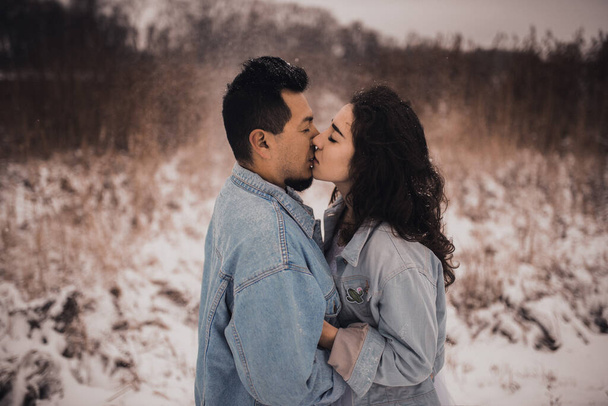 Мексиканський латиноамериканець у джинсовому піджаку завищений, а жінка цілується, обіймаючись, сміючись. Наречена і наречена кохають пару взимку у снігу. фешенебельне весілля 2021 року. - Фото, зображення