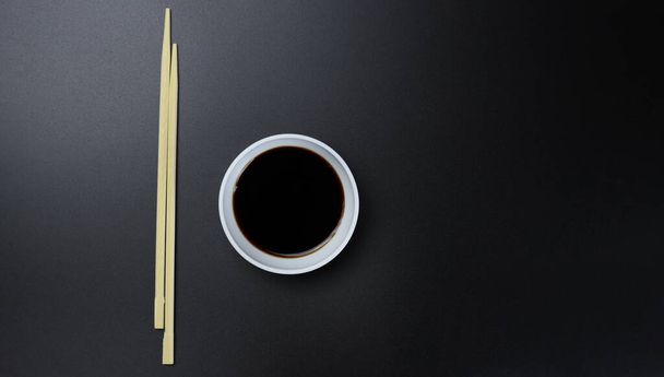 Деревянные палочки для еды, суши и кастрюли с соусом на черном фоне - Фото, изображение