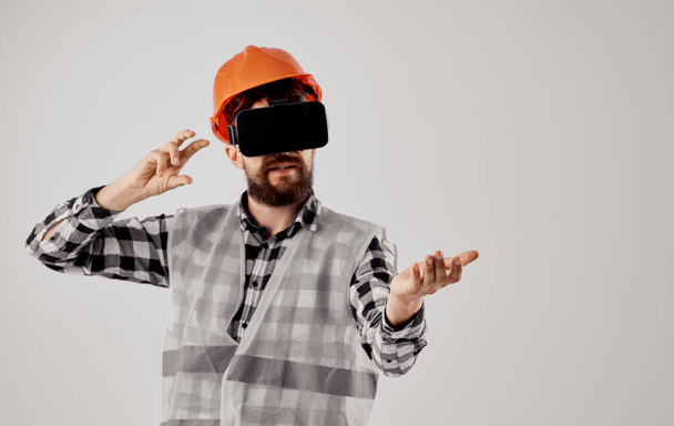 Ένας αρχιτέκτονας σε 3D γυαλιά εικονικής πραγματικότητας χειρονομίες με τα χέρια του και ένα πορτοκαλί κράνος στο κεφάλι του - Φωτογραφία, εικόνα