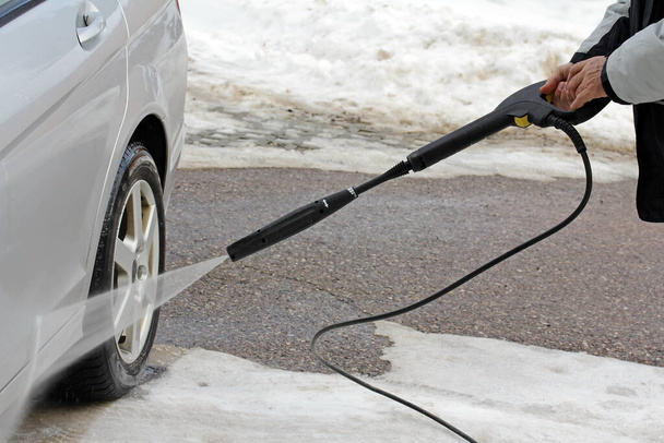 Un hombre lava la tierra y la sal de su coche en invierno.  - Foto, imagen