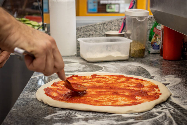 Un hombre haciendo una pizza margherita en un restaurante local de pizza y giroscopios - Foto, imagen