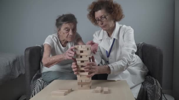 Terapia de demencia de manera lúdica, entrenamiento de dedos y habilidades motoras finas, construir bloques de madera en la torre, jugando Jenga. Mujer mayor de 90 años y médico jugando juego educativo en el hogar de ancianos - Metraje, vídeo