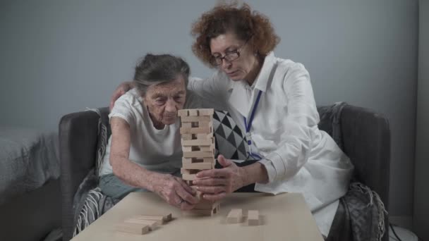 Senioren oefenen vaardigheden bouwen houten blokken, toren bouwen en proberen om het niet te laten vallen, Jenga spel. Oude patiënt uit te trekken blok, plaats op de top, ondersteuning dotor tijdens therapie dementie in huis - Video