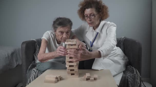 Зрілий лікар проводить сеанс, терапію для старшого пацієнта в будинку престарілих, тренує дрібні моторні навички для деменції, хвороби Альцгеймера та інституту відновлення шляхом складання дерев'яних блоків, граючи дженга
 - Кадри, відео