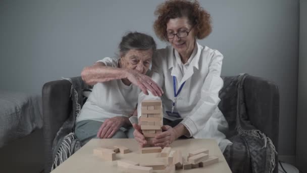 Mature doctor conducting session, therapy for senior patient in nursing home, training fine motor skills for dementia, alzheimer disease and recovery institute by folding wooden blocks, playing - Footage, Video