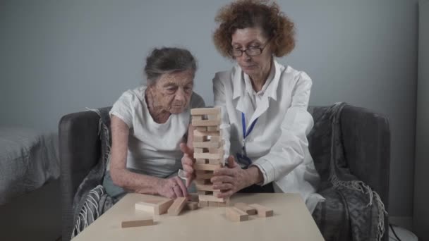 Зрілий лікар проводить сеанс, терапію для старшого пацієнта в будинку престарілих, тренує дрібні моторні навички для деменції, хвороби Альцгеймера та інституту відновлення шляхом складання дерев'яних блоків, граючи дженга
 - Кадри, відео