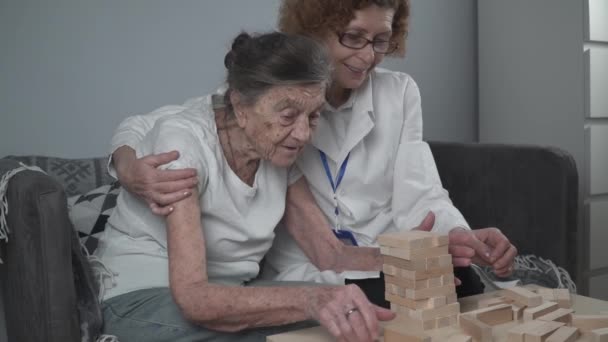 Зрелый врач проводит сеанс, терапию для пожилого пациента в доме престарелых, обучение мелкой моторике для слабоумия, болезни Альцгеймера и восстановительного института, складывая деревянные блоки, играя в дженгу - Кадры, видео