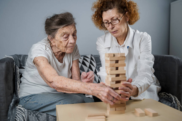 Érett orvos vezető ülés, terápia idős betegek idősek otthonában, képzés finom motoros készségek demencia, Alzheimer-kór és helyreállítási intézet hajtogatott fa blokkok, játék jenga. - Fotó, kép