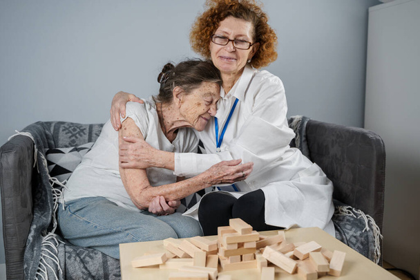 Mecz Jengi. Tematem jest demencja, starzenie się i zabawy dla starszych ludzi. Kaukaska seniorka buduje wieżę z drewnianych klocków z pomocą lekarza w ramach terapii i gry jenga w domu pacjenta. - Zdjęcie, obraz