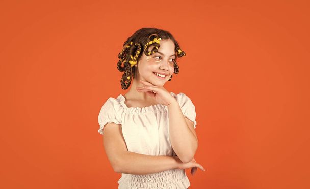 Child making hairstyle. little happy girl with curlers in hair. fabric mask under eyes for beauty. cute kid standing with patches under eyes. Child fashion model concept. Curled hair with braid. - Fotó, kép