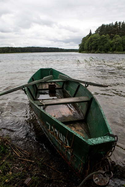 Drewniana łódź wiosłowa na brzegu jeziora. Scena spokoju nad jeziorem Baluosas w etnograficznej wiosce Suminai, Litwa - Zdjęcie, obraz