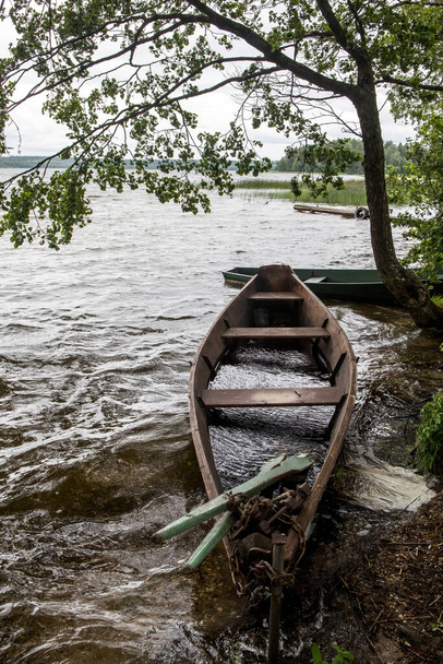 Dřevěný veslařský člun na břehu jezera. Klidná scéna na jezeře Baluosas v etnografické vesnici Suminai, Litva - Fotografie, Obrázek